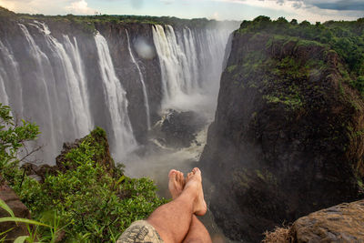 Low section of man sitting against waterfall