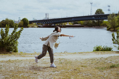 Full length of young woman throwing water from bottle near river