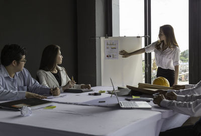 Businesswoman giving presentation while colleagues sitting at table in office