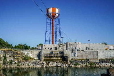 Water tower by river against clear blue sky