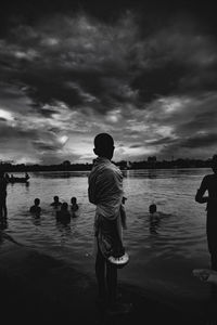 Rear view of silhouette boy standing in lake against sky