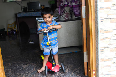 Full length portrait of cute boy with push scooter on floor at home