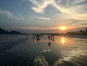 People at beach against sky during sunset