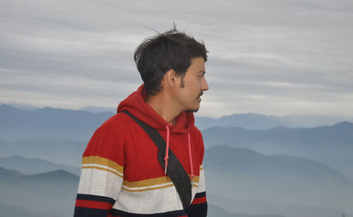 Close up of a handsome young guy looking sideways while posing against the background of mountains 