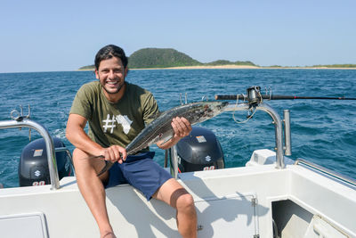 Portrait of smiling man holding dead fish while sitting on boat sailing in sea