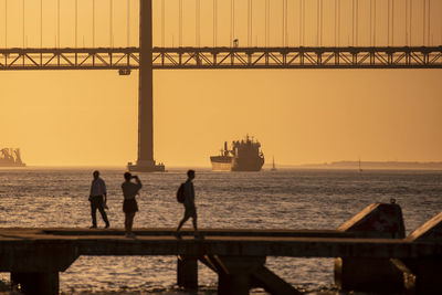 Silhouette people on pier on sea against sky during sunset