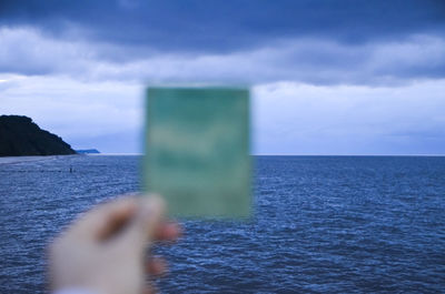 Cropped image of person holding photograph against baltic sea