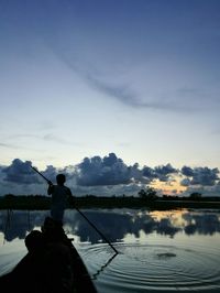 Rear view of silhouette man fishing in lake against sky