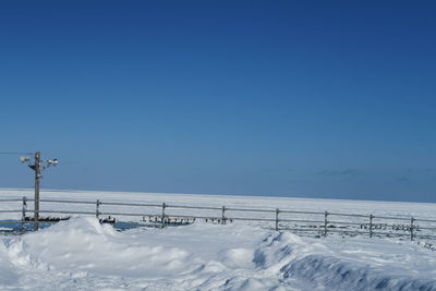 Snow covered land against clear blue sky