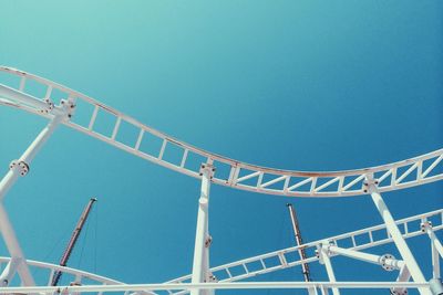 Low angle view of white rollercoaster against clear blue sky