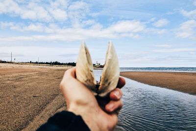 Close-up of hand holding ice cream at beach against sky