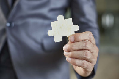 Midsection of businessman holding jigsaw piece at office