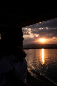 Woman looking at sea against sky during sunset