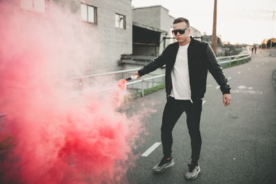 Full length of young man holding distress flare on road