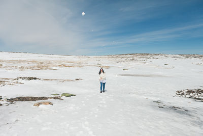 Woman walking on snow field against blue sky