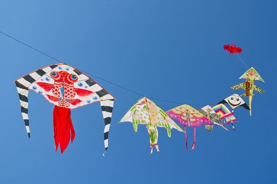 Low angle view of kites hanging against clear blue sky