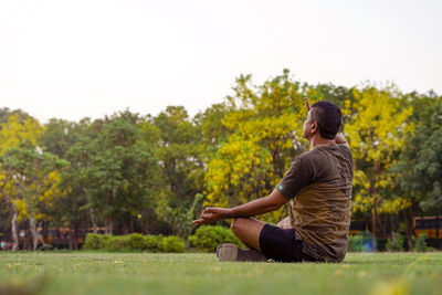 Side view of woman sitting on grass against trees