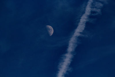 Low angle view of vapor trail in sky and moon 