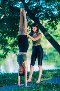 Women doing yoga by the water. instructor helping woman to do headstand.