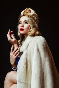 Beautiful woman wearing fur jacket and crown against black background