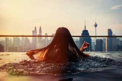 Rear view of woman swimming in infinity pool at city