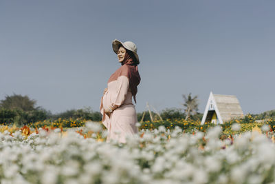 Woman standing by flowering plants on field against sky