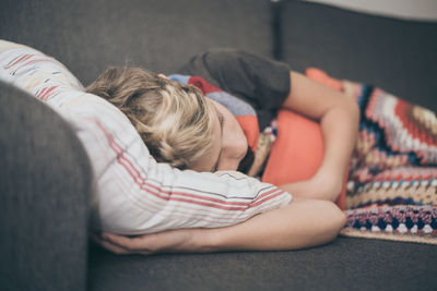 Ill boy sleeping with hot water bottle on sofa