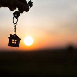 Silhouette of a house figure with a key, a pen with a keychain on the background of the sunset. 