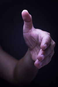 Cropped hand gesturing sign against black background