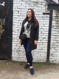 Full length portrait of young woman standing against brick wall