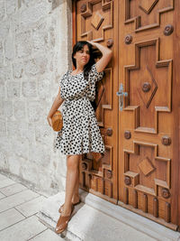 Portrait of beautiful young woman in polka dot dress in front of wooden door.