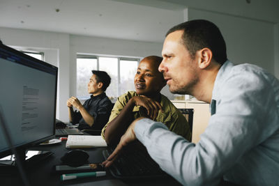 Businessman using computer while sitting with female colleague at office