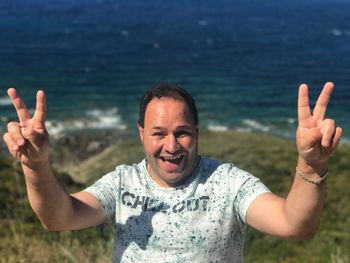 Portrait of cheerful man gesturing peach sign at corsica beach