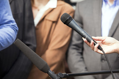 Cropped hand of woman holding microphone in front of people