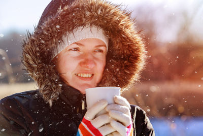 Woman drinking coffee standing outdoors during snowfall