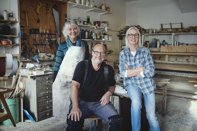 Portrait of smiling male and female senior colleagues standing against tools at workshop