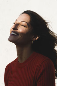 Young brunette woman laughing against wall on sunny day