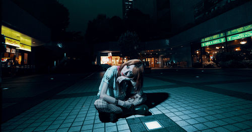 Portrait of man sitting on footpath at night