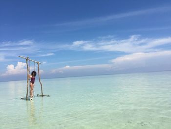 Woman standing on swing over sea against sky