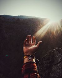 Cropped hand of man gesturing on mountain towards sky during sunny day