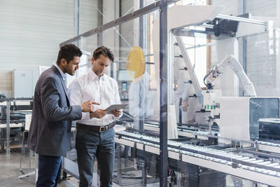 Two businessmen with tablet talking in modern factory