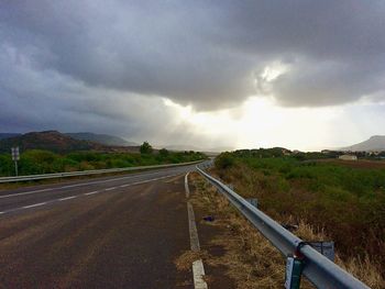 Empty road on countryside landscape against cloudy sky