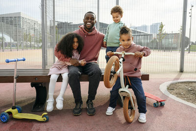 Happy father sitting with arm around children at sports field