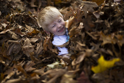 Cheerful boy lying amidst fallen dry leaves during autumn