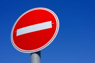 Low angle view of road sign against clear blue sky