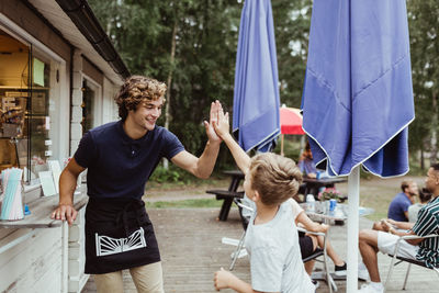 Smiling young owner giving high-five to customer while standing by restaurant