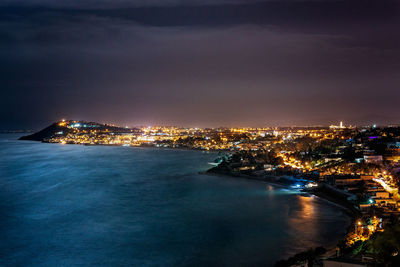 High angle view of illuminated buildings by sea against sky at night