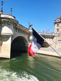 Flag over canal by bridge against clear sky