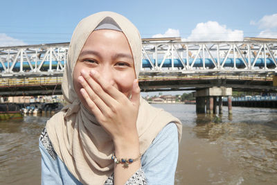 Portrait of young woman against river