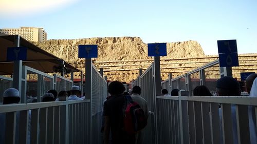 Rear view of people standing on railing against clear sky